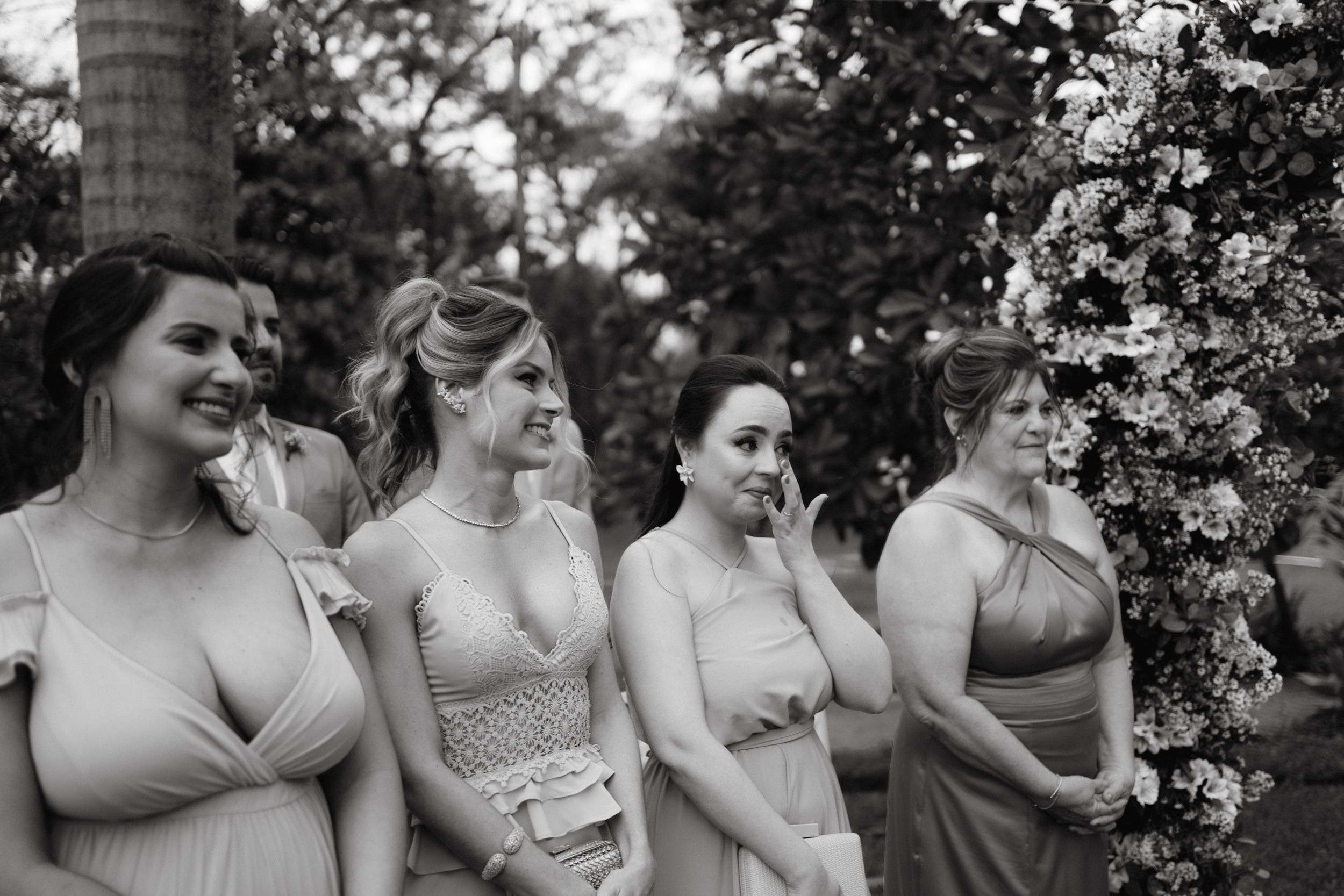 Bridesmaids in gray dresses stand together under blooming trees at outdoor wedding.