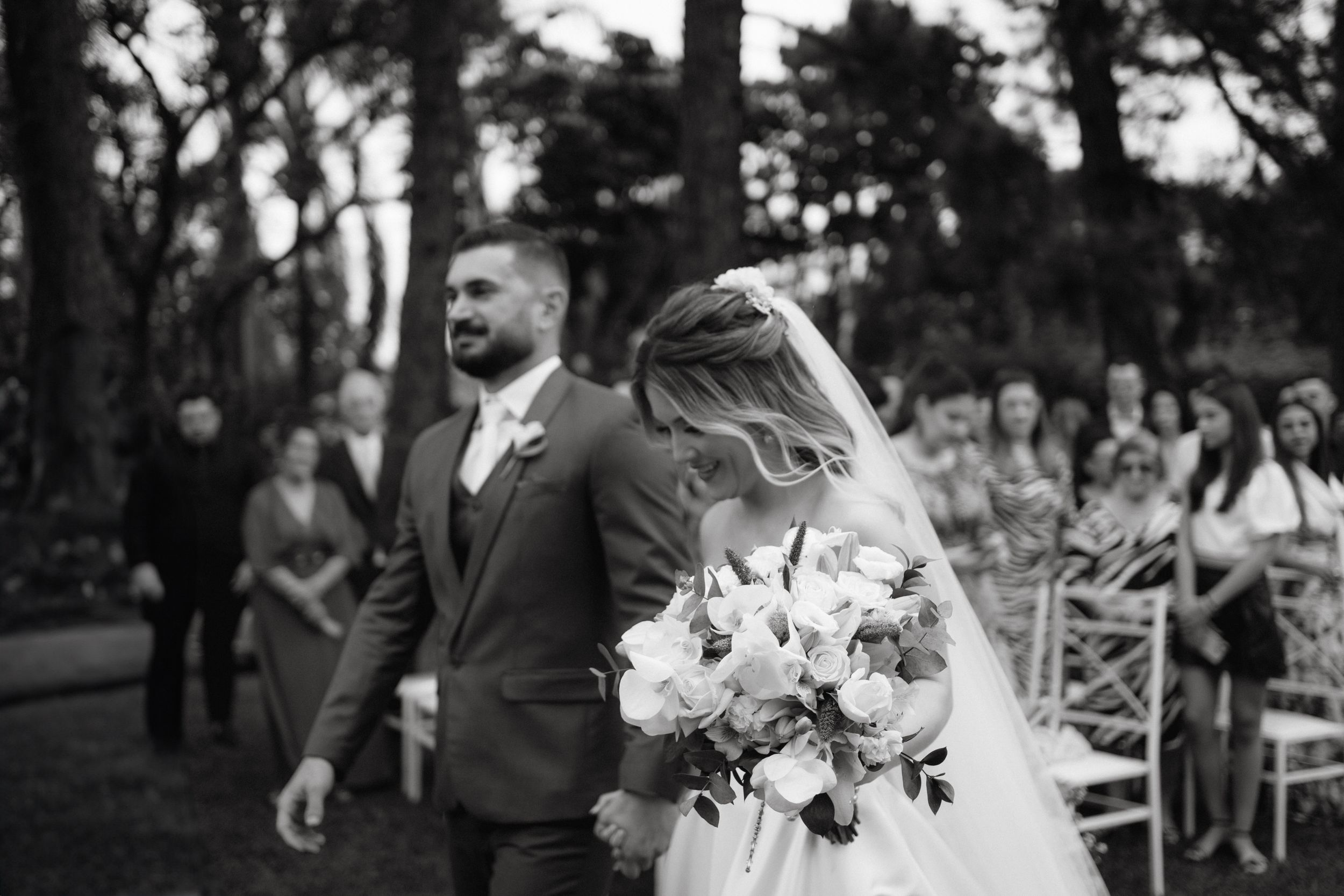 Wedding ceremony in a garden setting with white floral arrangements and cross-back chairs.