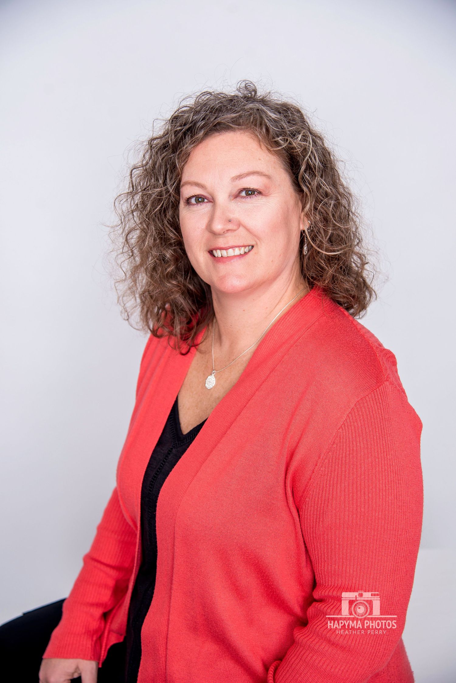 Professional headshot showing someone in a bright coral cardigan against a light gray background.