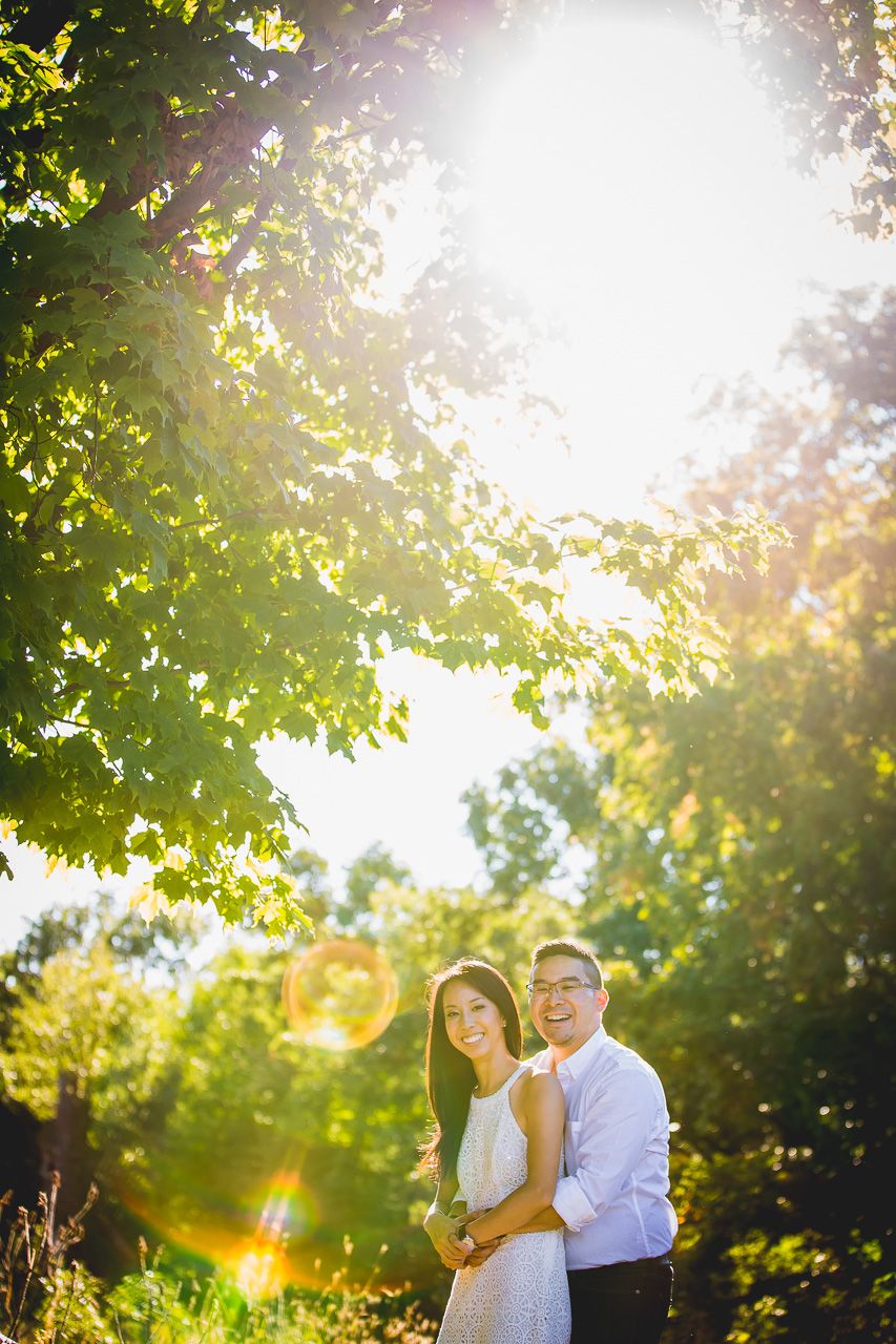 A romantic couple embraces in a sunlit garden with lens flare and green foliage creating a dreamy atmosphere.