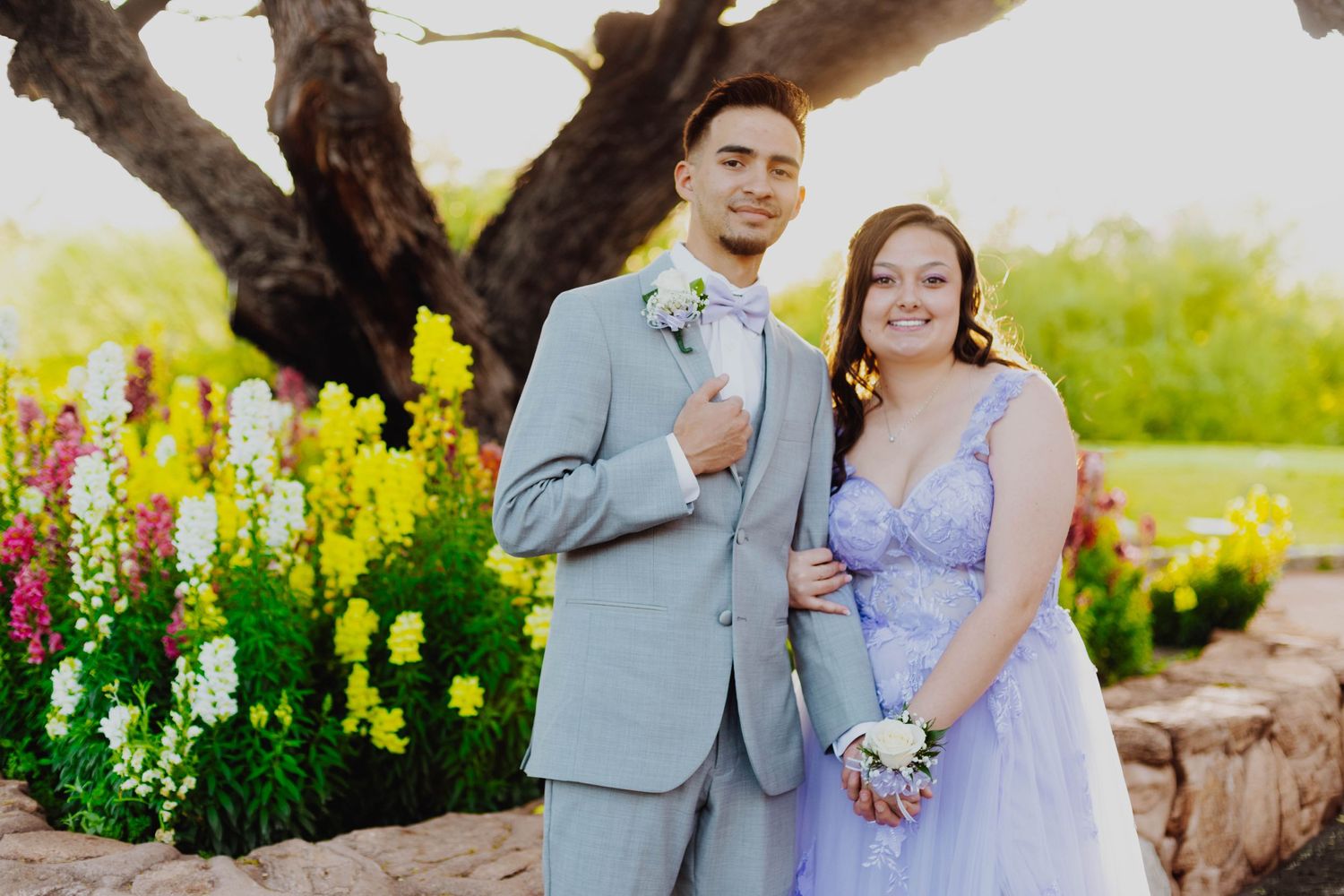 Couple in formal attire poses against garden backdrop with colorful snapdragon flowers.