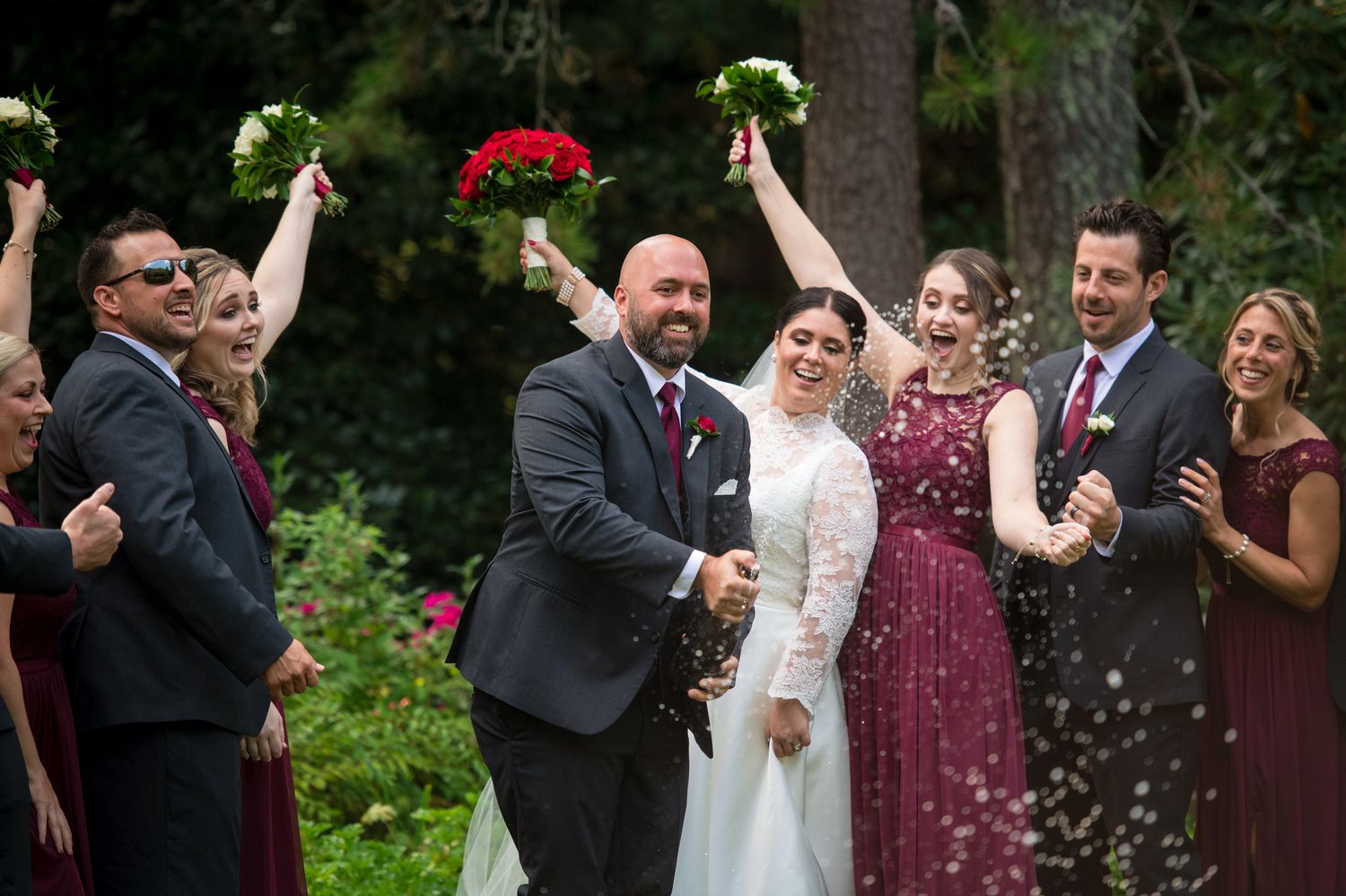 Wedding party celebrates with raised bouquets during an outdoor garden ceremony.