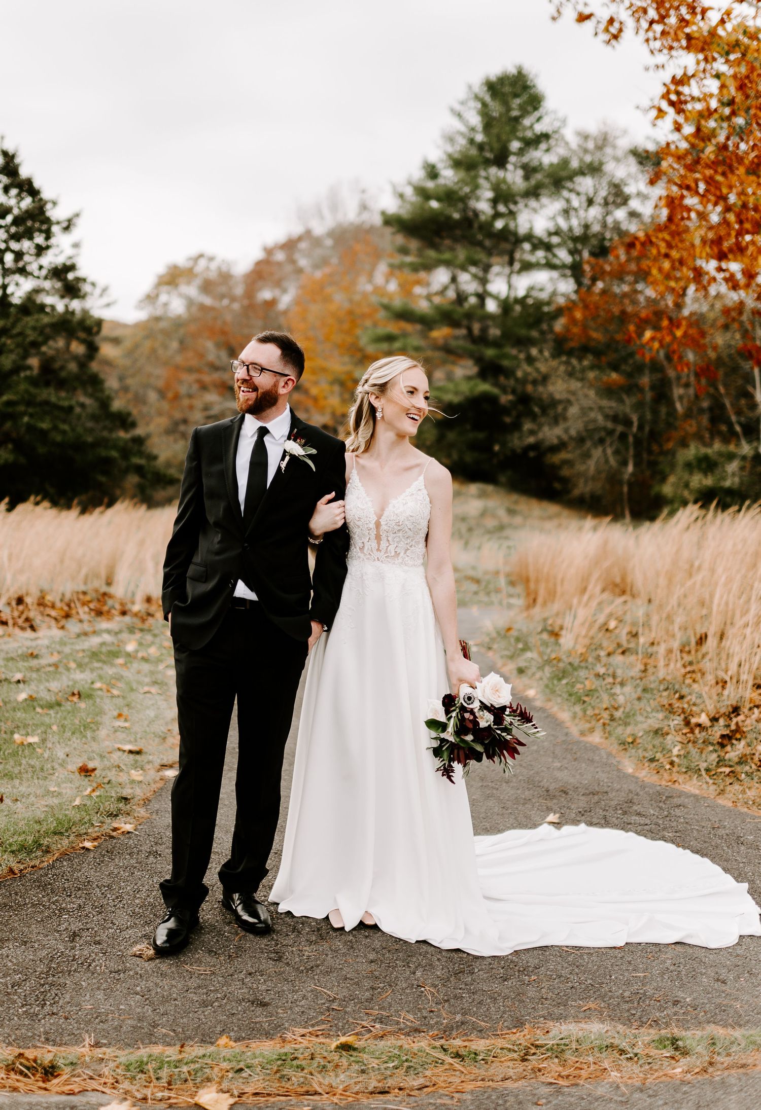 Couple walking together on winding path surrounded by fall foliage and tall grass.