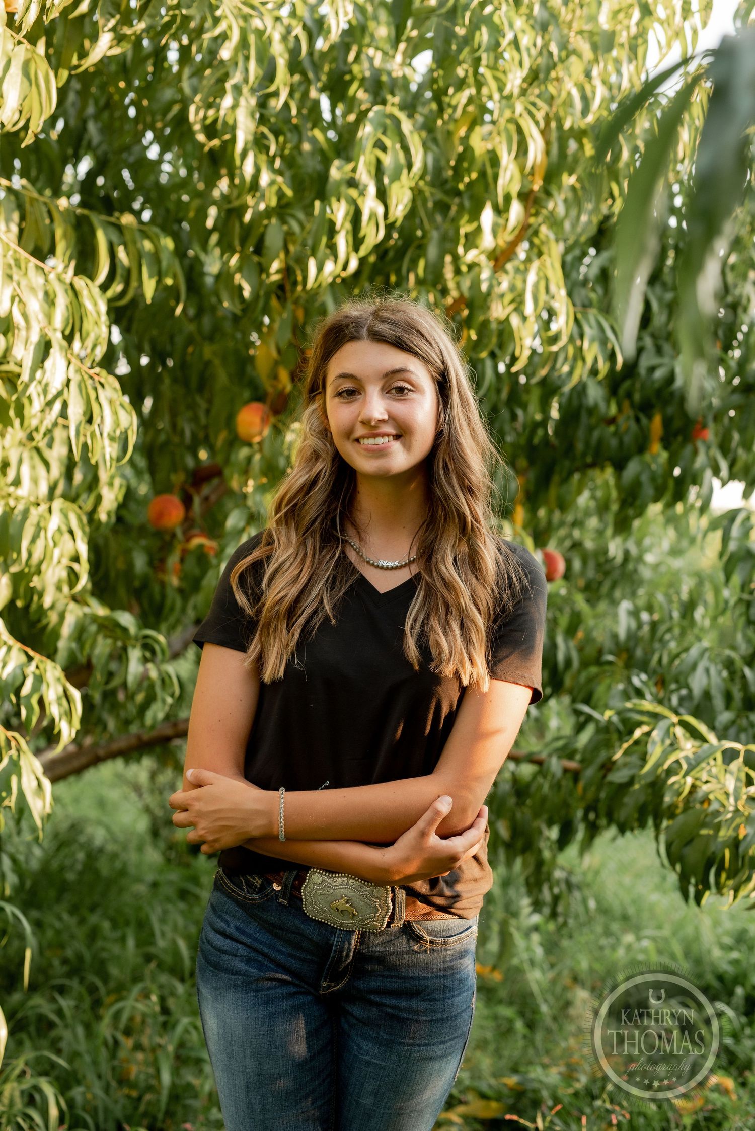 Relaxed outdoor portrait against lush peach trees in warm evening light.