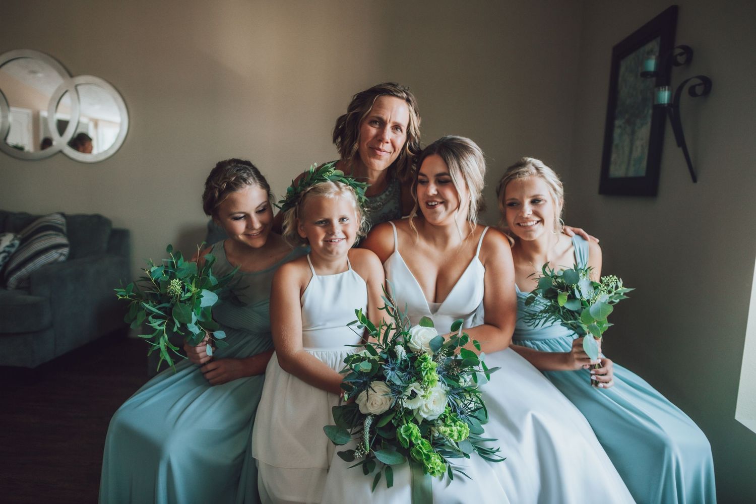 Wedding party in light blue dresses poses together holding green and white bouquets.