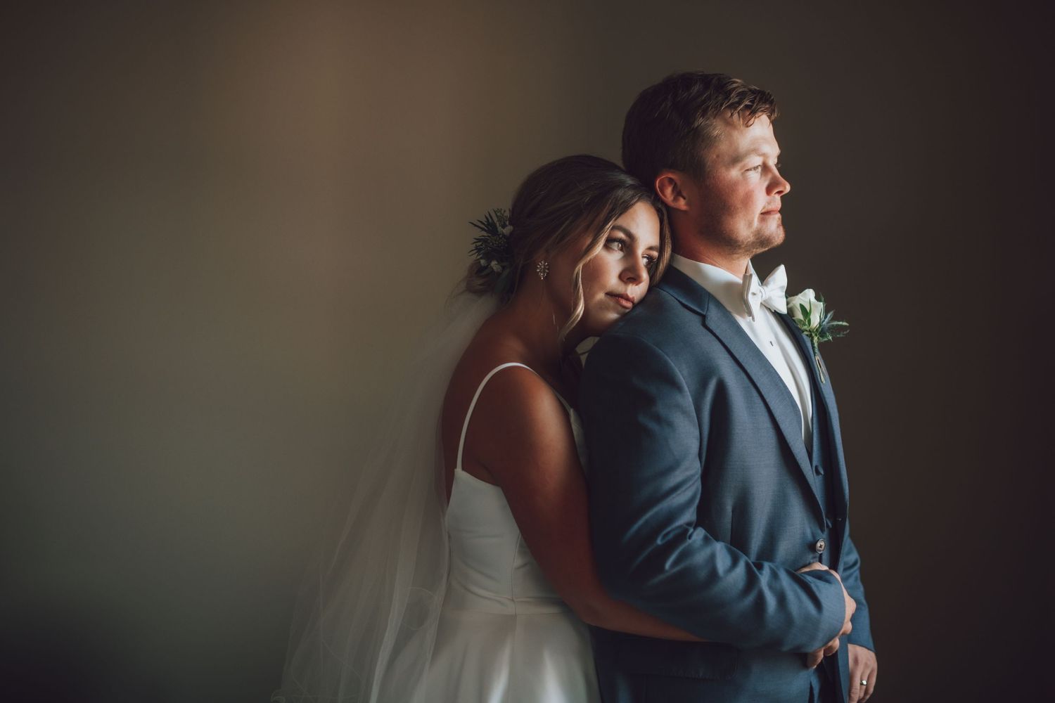 Intimate wedding moment captured in dark moody lighting with elegant floral bouquet.