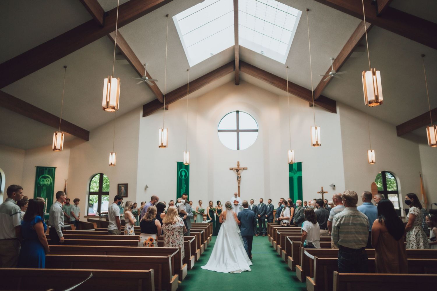 Church wedding ceremony in panoramic view with wooden beams and hanging pendant lights.