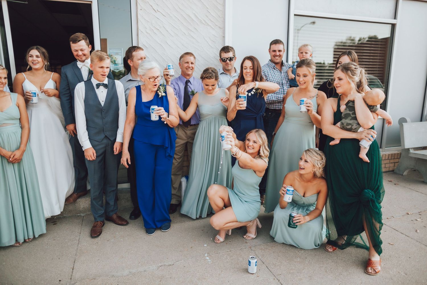 Large wedding party poses together outdoors wearing blue and gray attire.