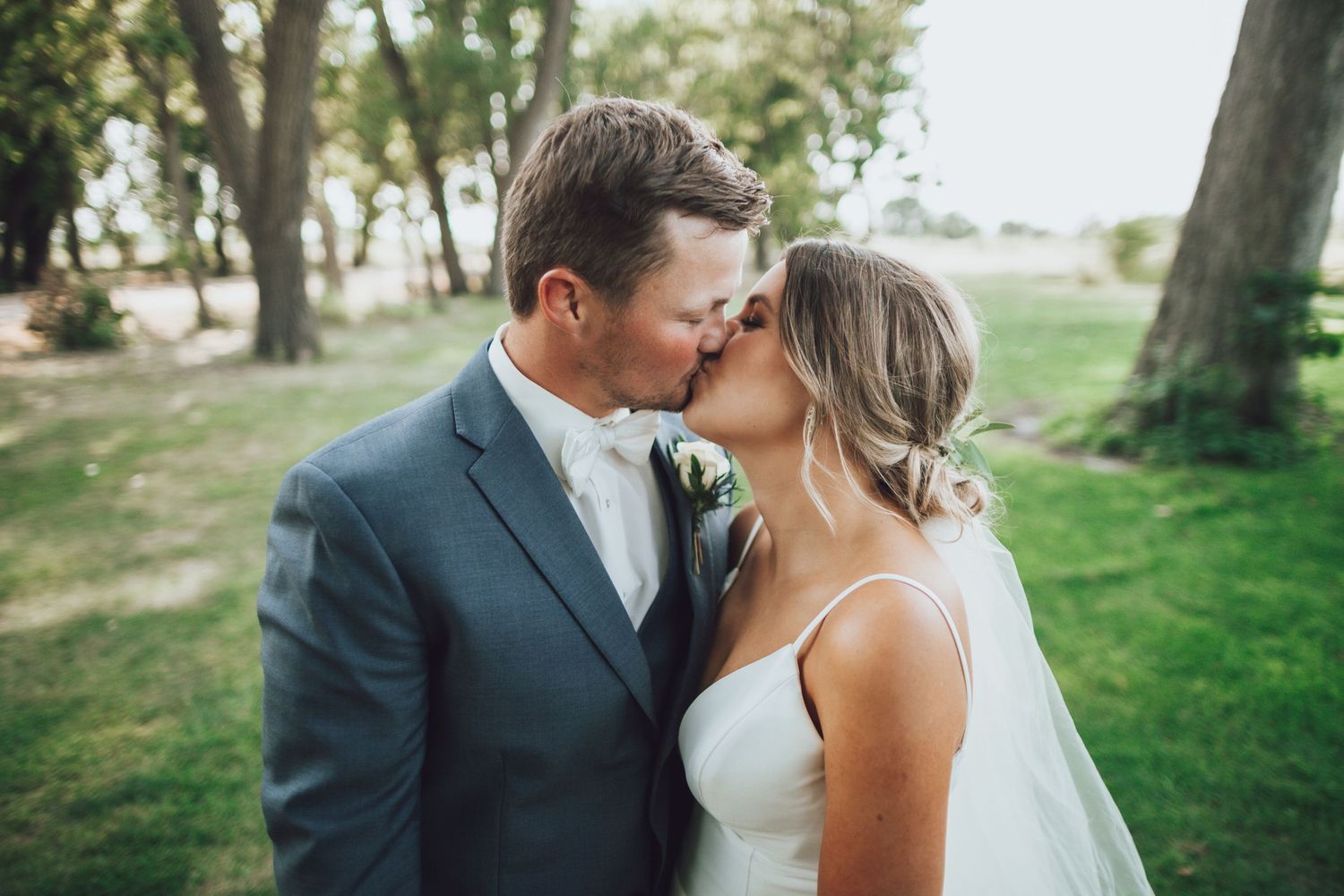 A romantic outdoor wedding moment with a couple sharing a tender kiss in a park setting.