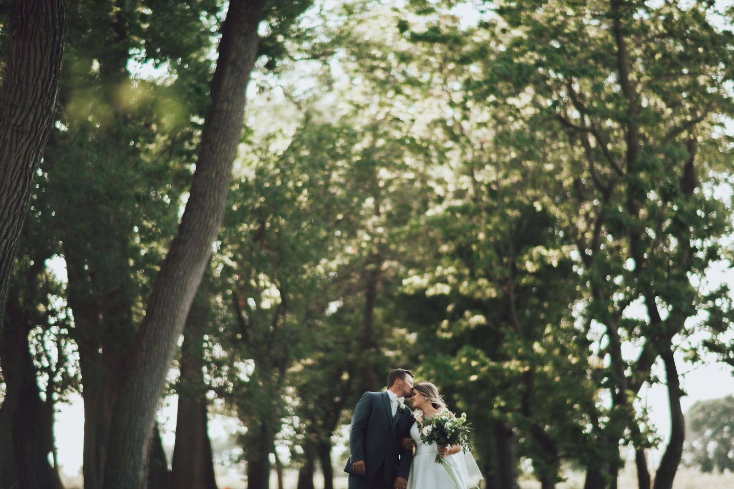 Wedding party poses playfully outdoors among trees in mint green dresses and navy suits.
