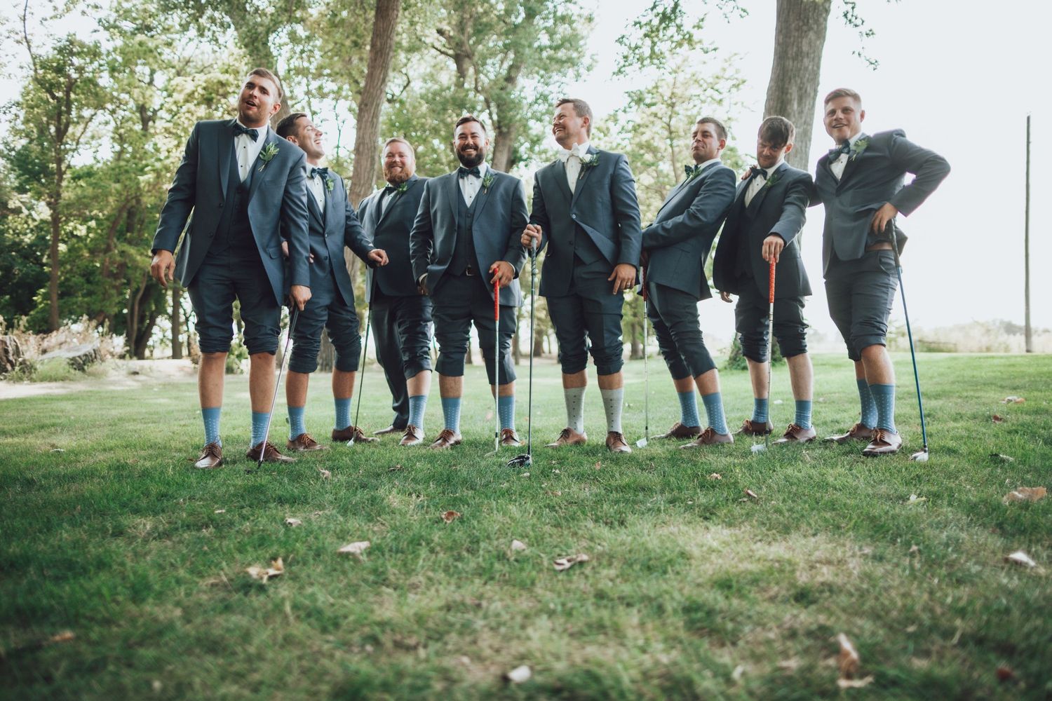 Wedding party members line up showing off their socks in a playful outdoor photo.