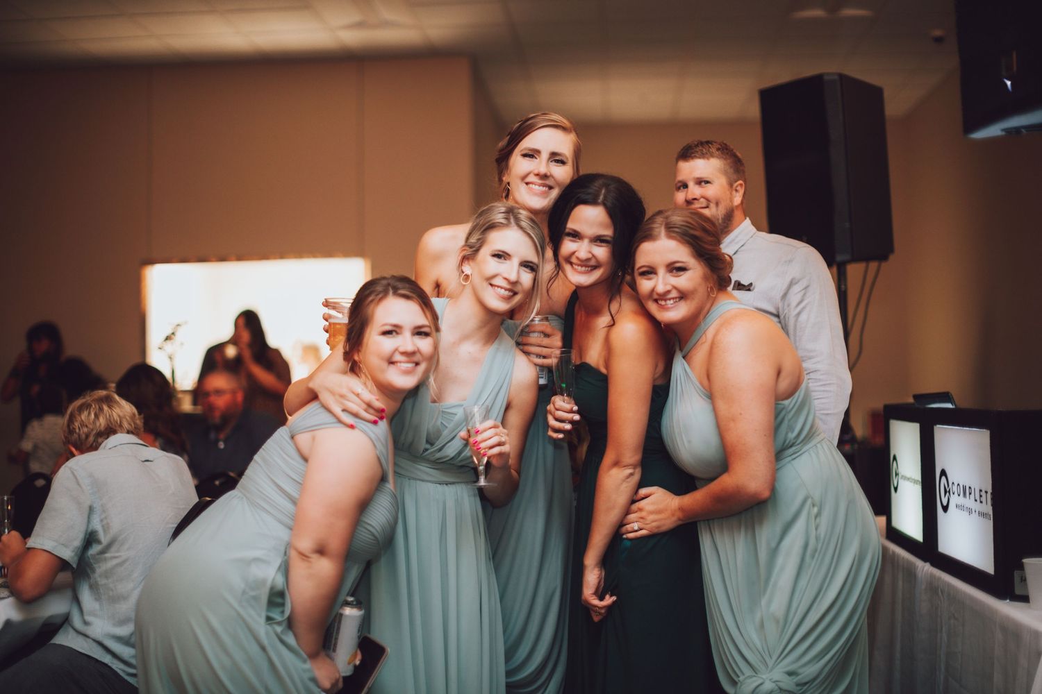 Wedding party in mint green dresses dancing and celebrating at indoor reception.