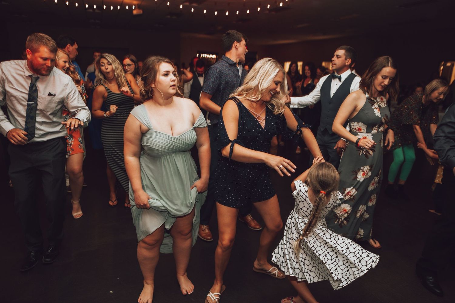 Wedding guests dancing and celebrating on a dimly lit dance floor at reception.