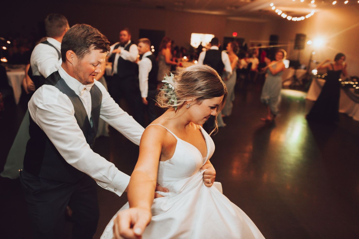 A couple dances joyfully at their wedding reception in a dimly lit ballroom.