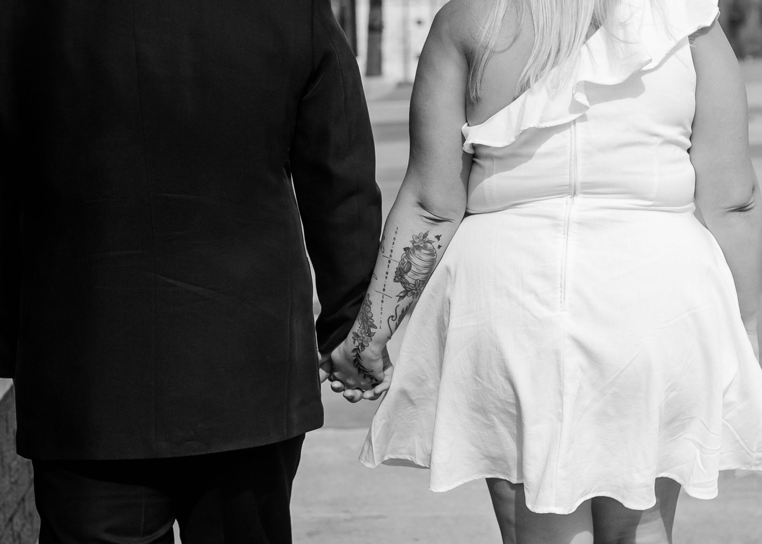 A black and white close-up of a couple holding hands while walking together.