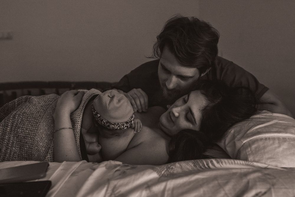 Two people share an intimate moment while lying on white bedding in soft lighting.