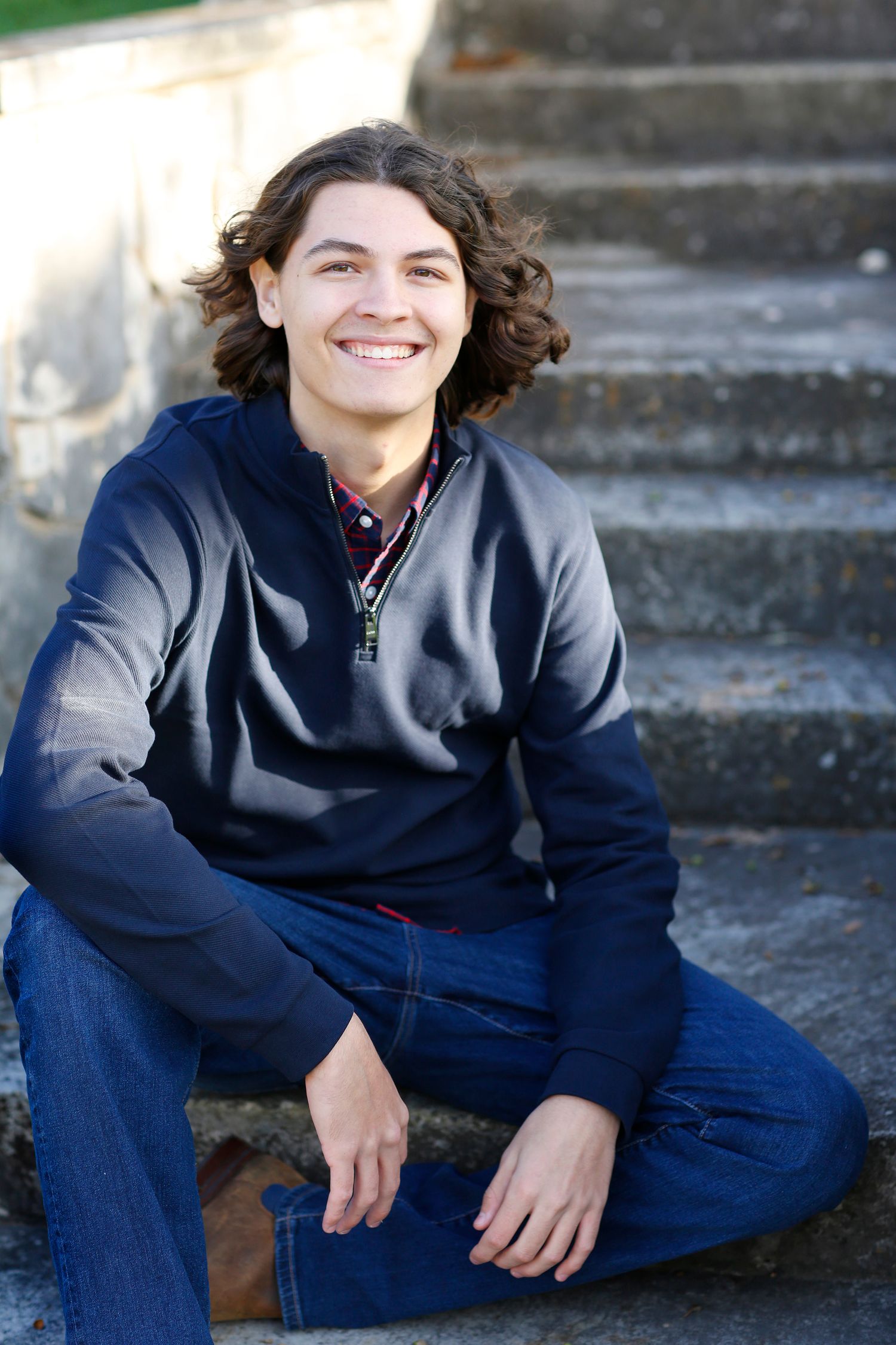 Casual portrait of person in blue sweater sitting on concrete steps outdoors.