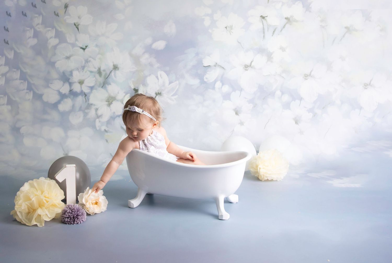 cake smash bath splash shoot, blue/grey floral backdrop, white victorian Bath, cream flowers & pom poms baby in Lilac