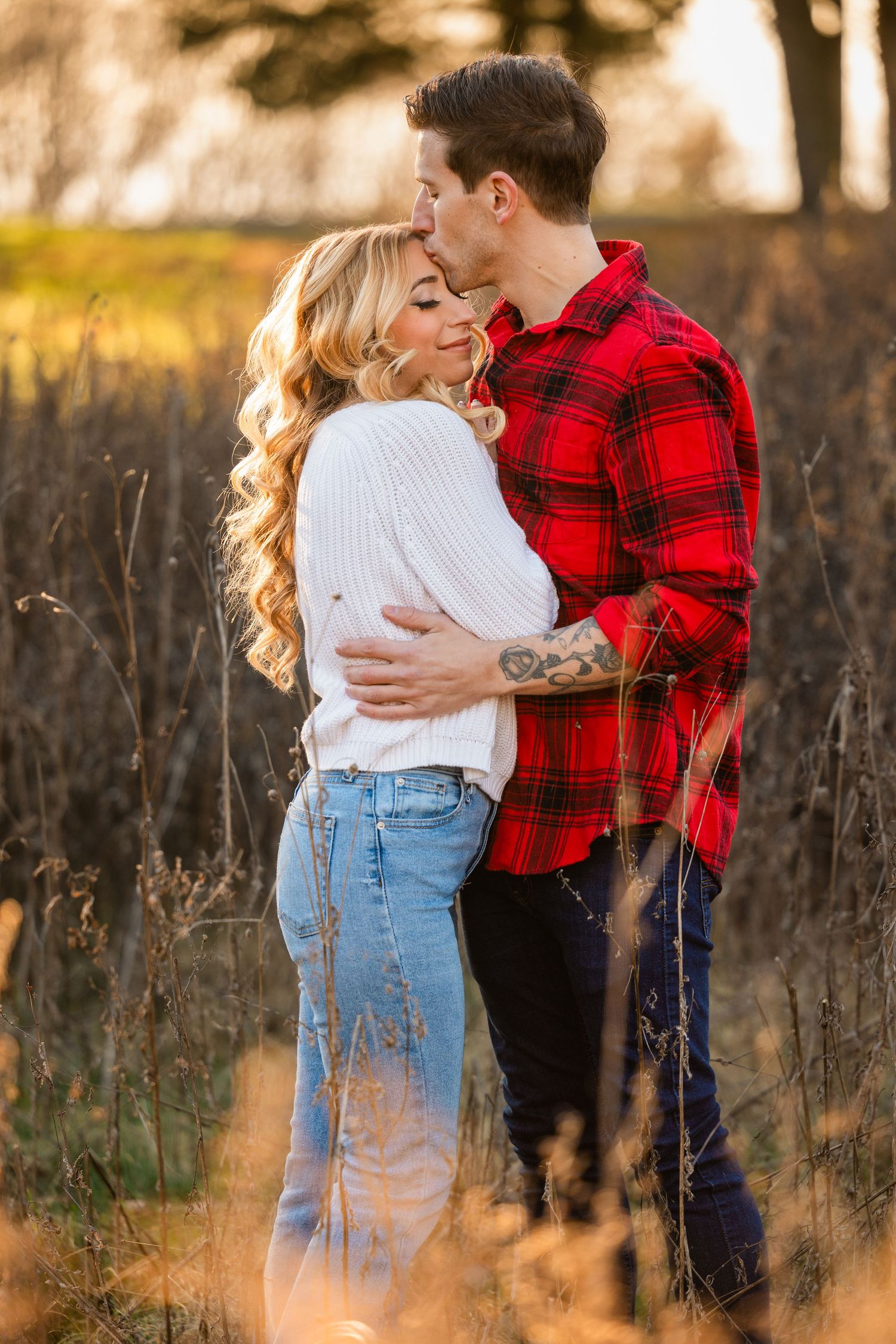 Intimate embrace in a field with soft sunset light filtering through autumn grass.