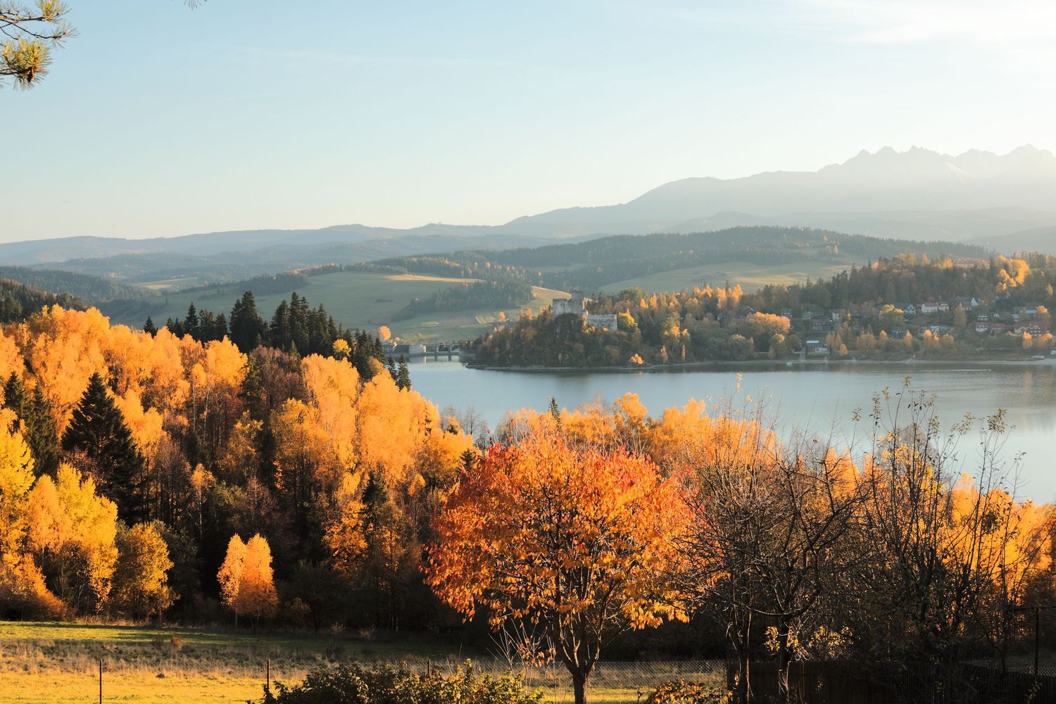 Panoramic autumn landscape with golden trees overlooking a lake and distant mountains.