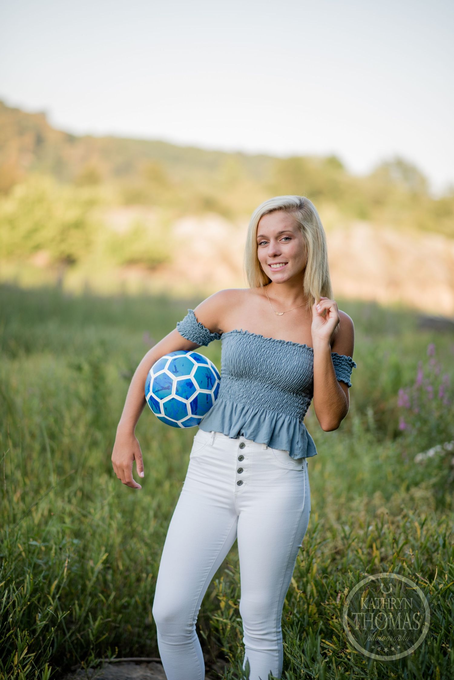Athletic photo shoot featuring a blue soccer ball and casual summer outfit in a field setting.