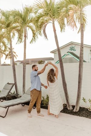 A couple dances together on a tropical patio with palm trees swaying above.