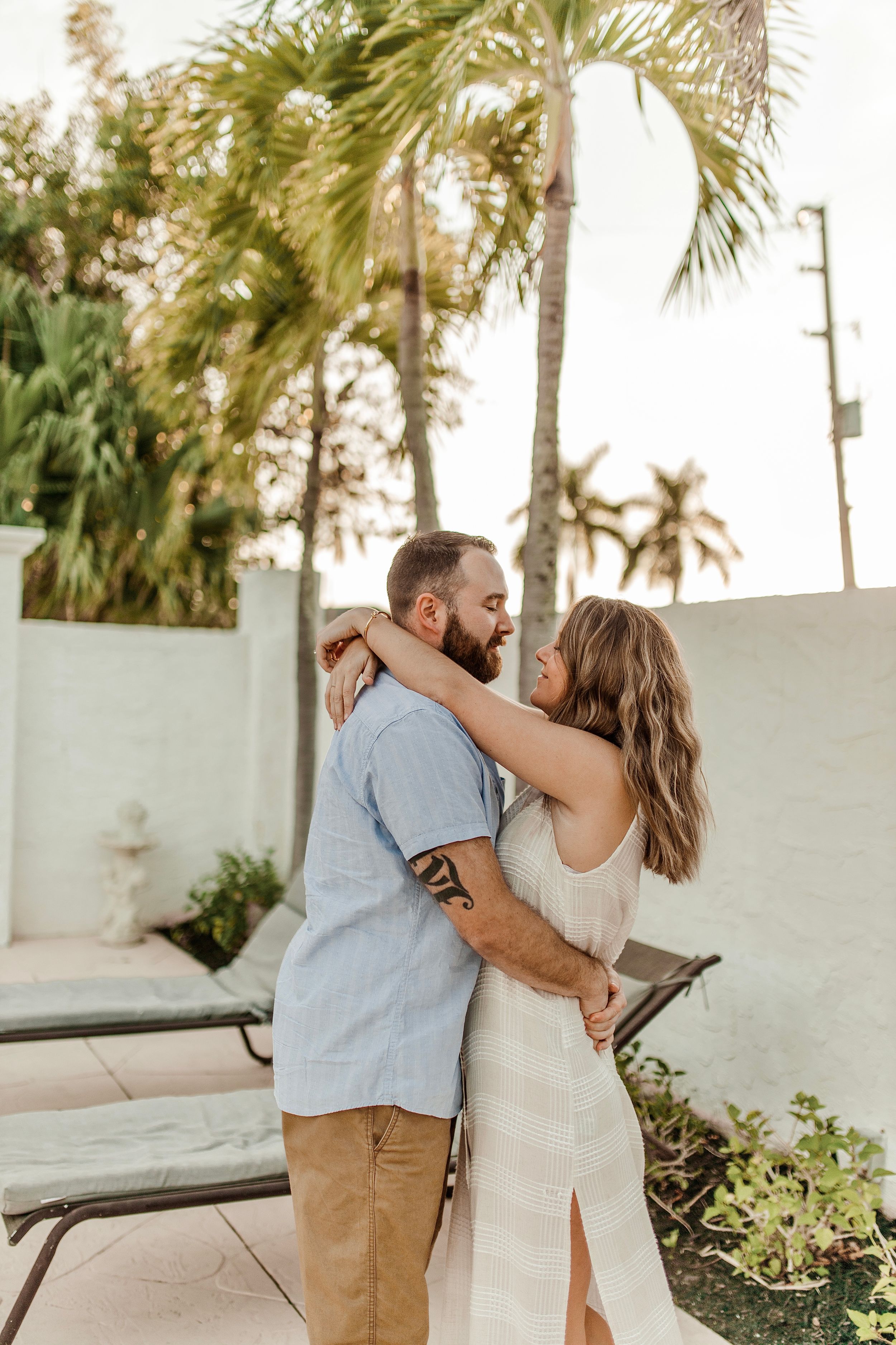 A couple embraces in warm sunlight on a tropical patio with palm trees overhead.