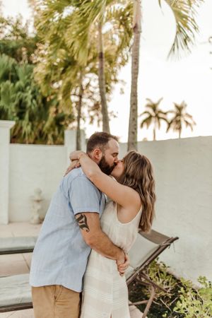 Romantic couple sharing an intimate kiss surrounded by palm trees in a tropical setting.