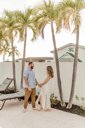A couple holds hands while standing on a patio surrounded by palm trees at a resort.