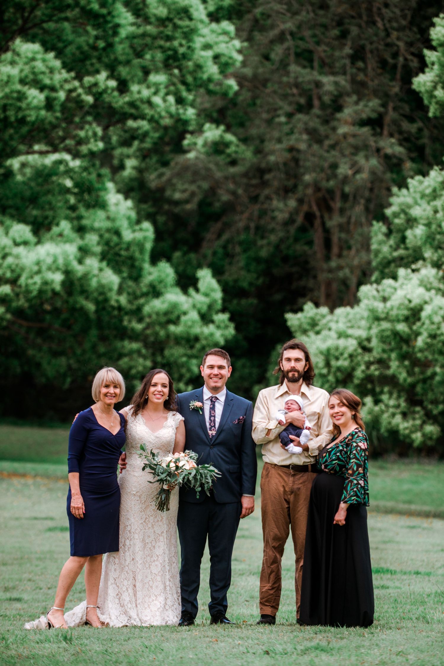 Wedding party poses for a formal photo in front of a green forest backdrop.