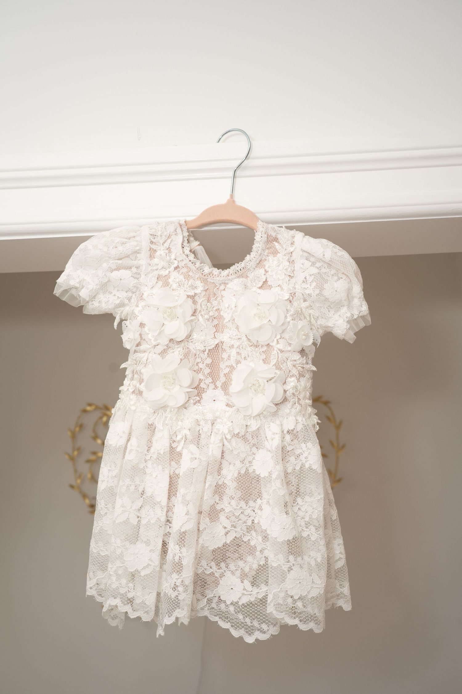 Delicate white lace christening dress hanging on display.