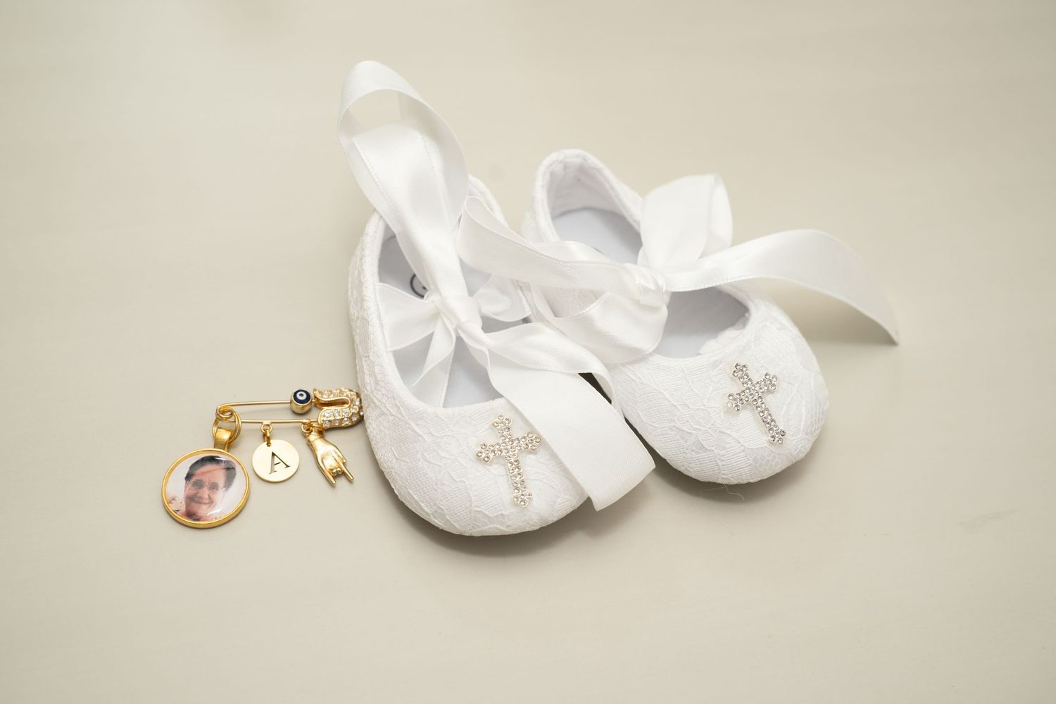 White baby shoes and religious jewelry arranged on cream background.