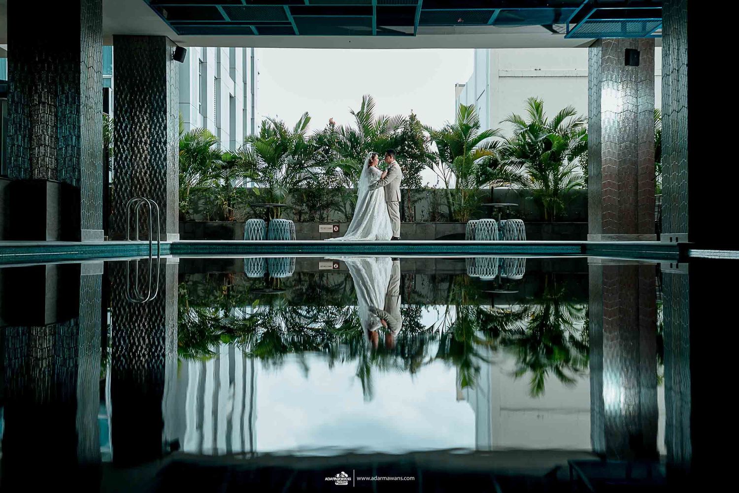 Wedding couple's reflection in glossy floor with palm trees and modern architecture in background.