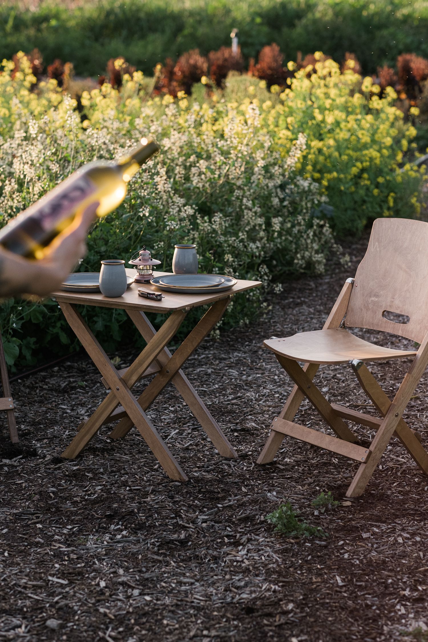 Wooden folding chairs set up in a garden with yellow wildflowers blooming in the background.