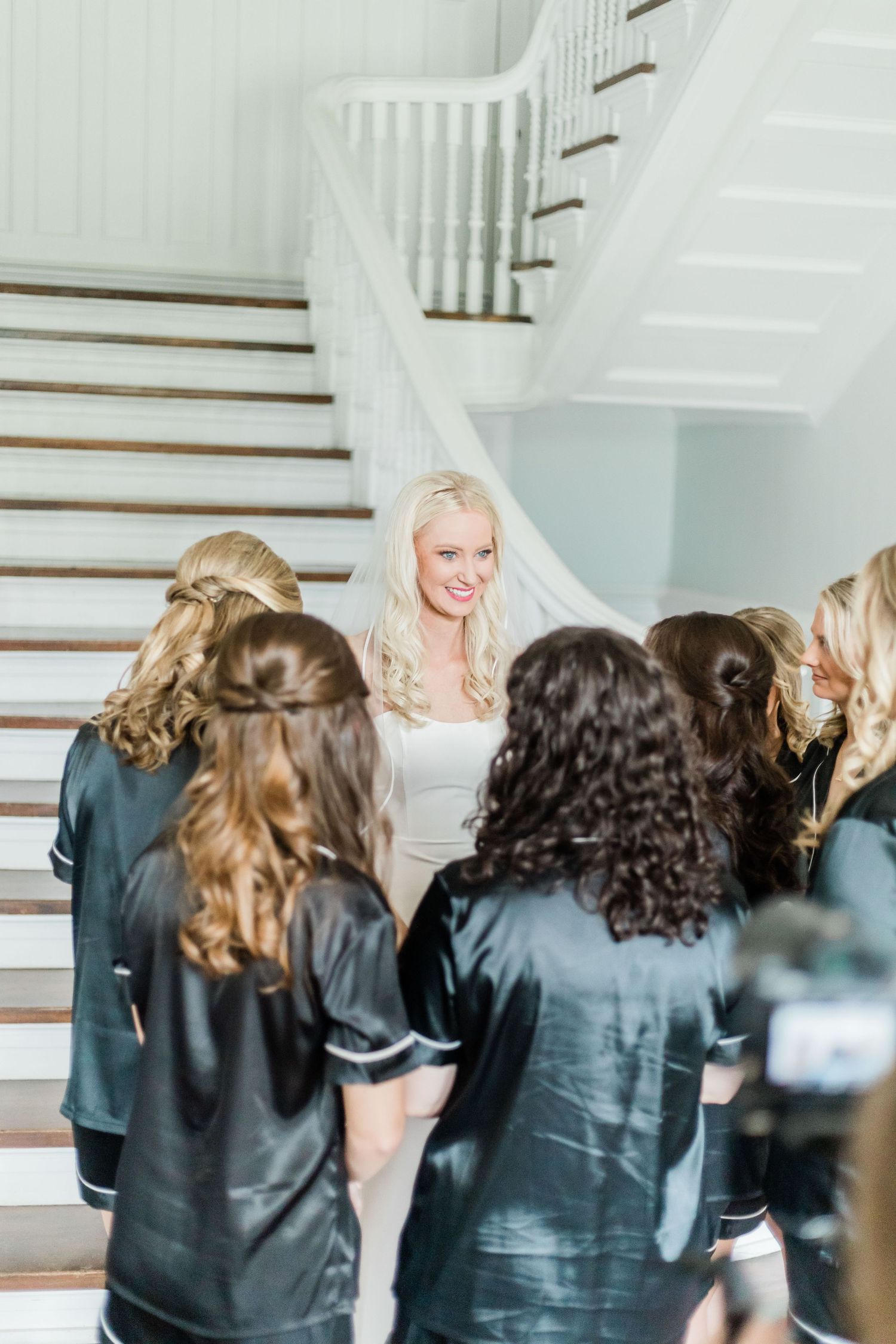 Bridesmaids in navy robes gathered around on an elegant white staircase.