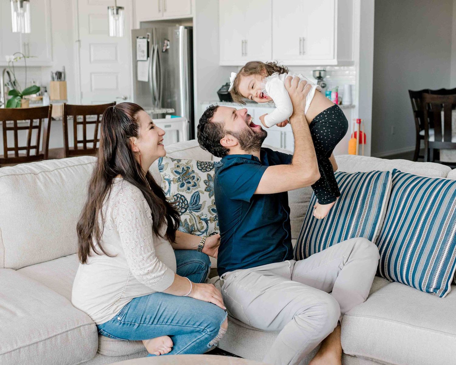 A happy family moment on a gray couch in a modern white living room.