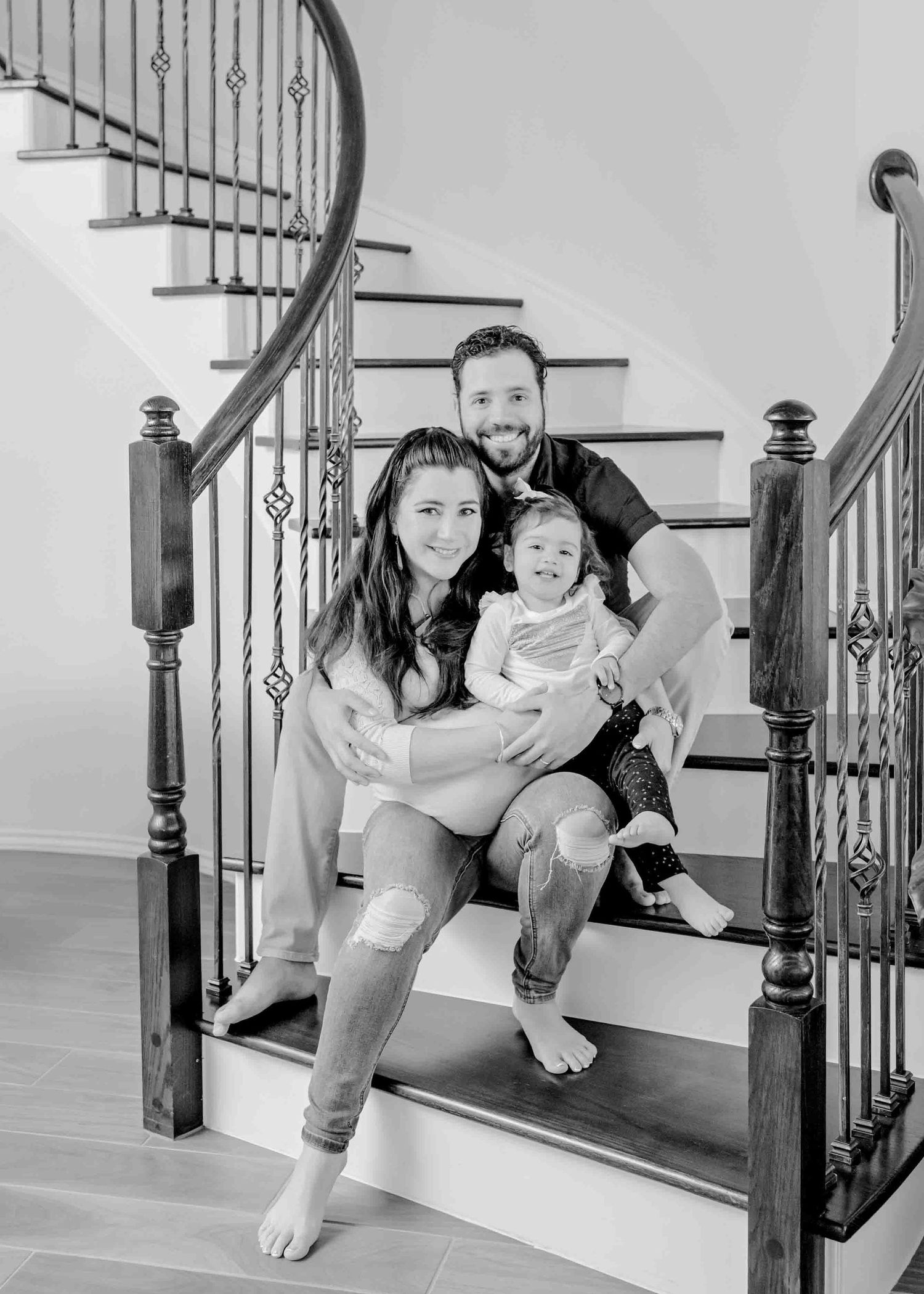 A family sitting together on wooden stairs with wrought iron railings in a bright home.
