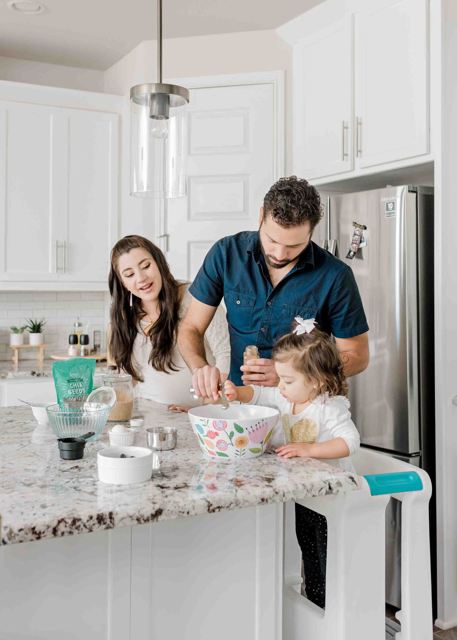 A family baking together at a granite kitchen counter with white cabinets.