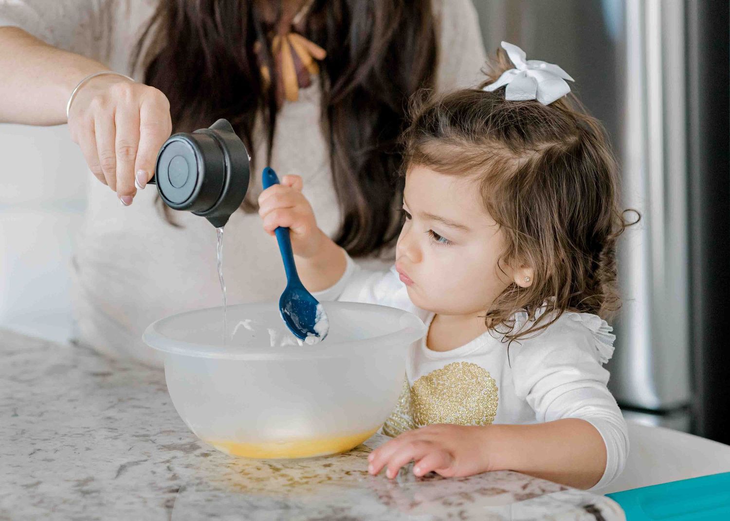 A young child helps mix ingredients in a white bowl while baking.