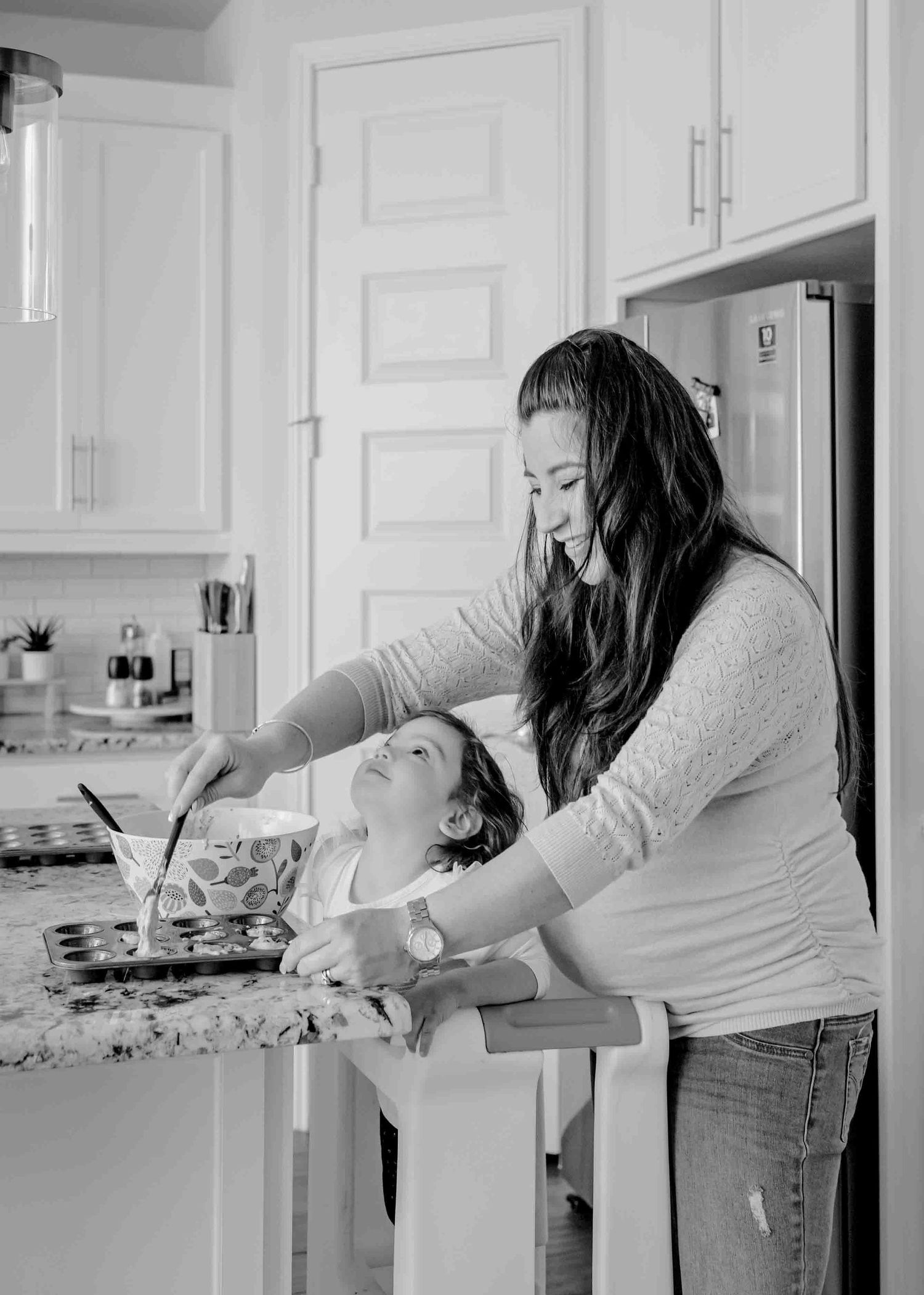 Black and white photo of a cooking moment in a modern kitchen with a toddler helping.