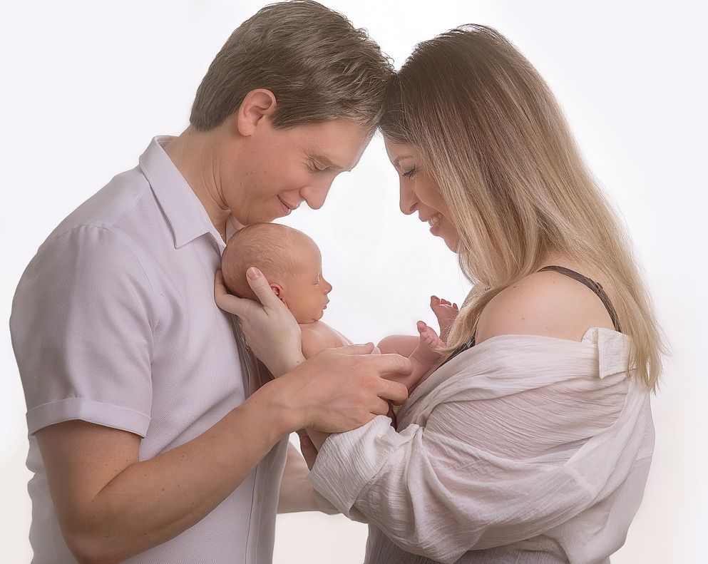 Intimate family portrait of parents with their newborn baby against white background.
