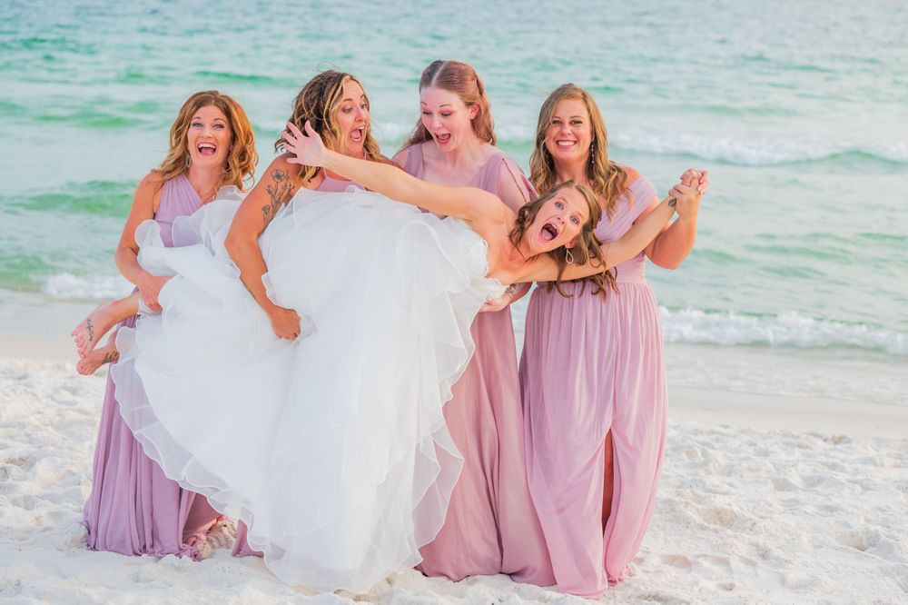 fun bridesmaids portrait holding up the bride on her wedding day on the beach at sunset on Panama City Beach Florida