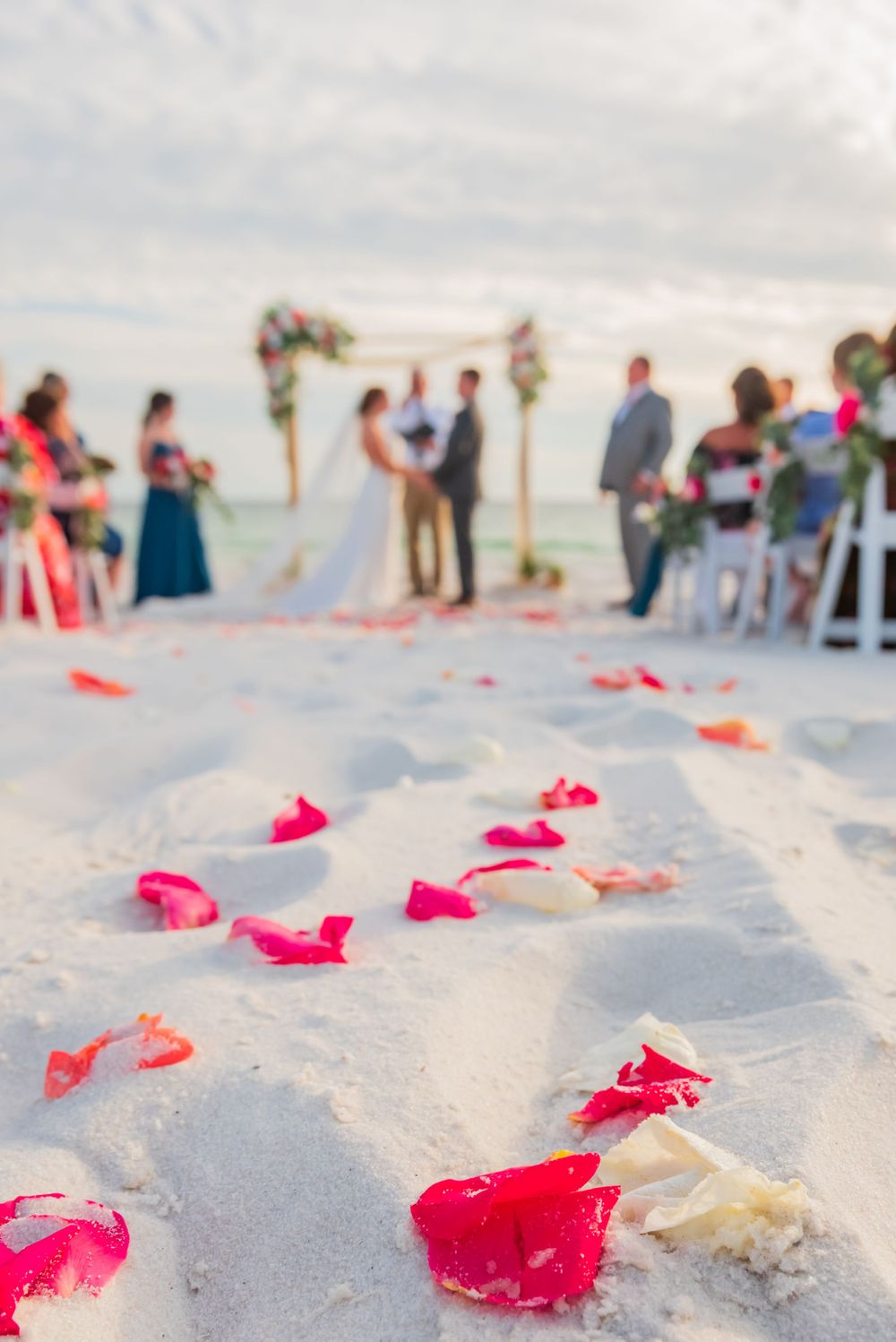rose petals in the sand with bride & groom in the background  beach wedding ceremony on Panama City beach Florida sunset
