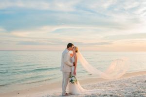 bride & groom kissing at sunset on their wedding day on Panama City Beach Florida as her veil blows in the wind