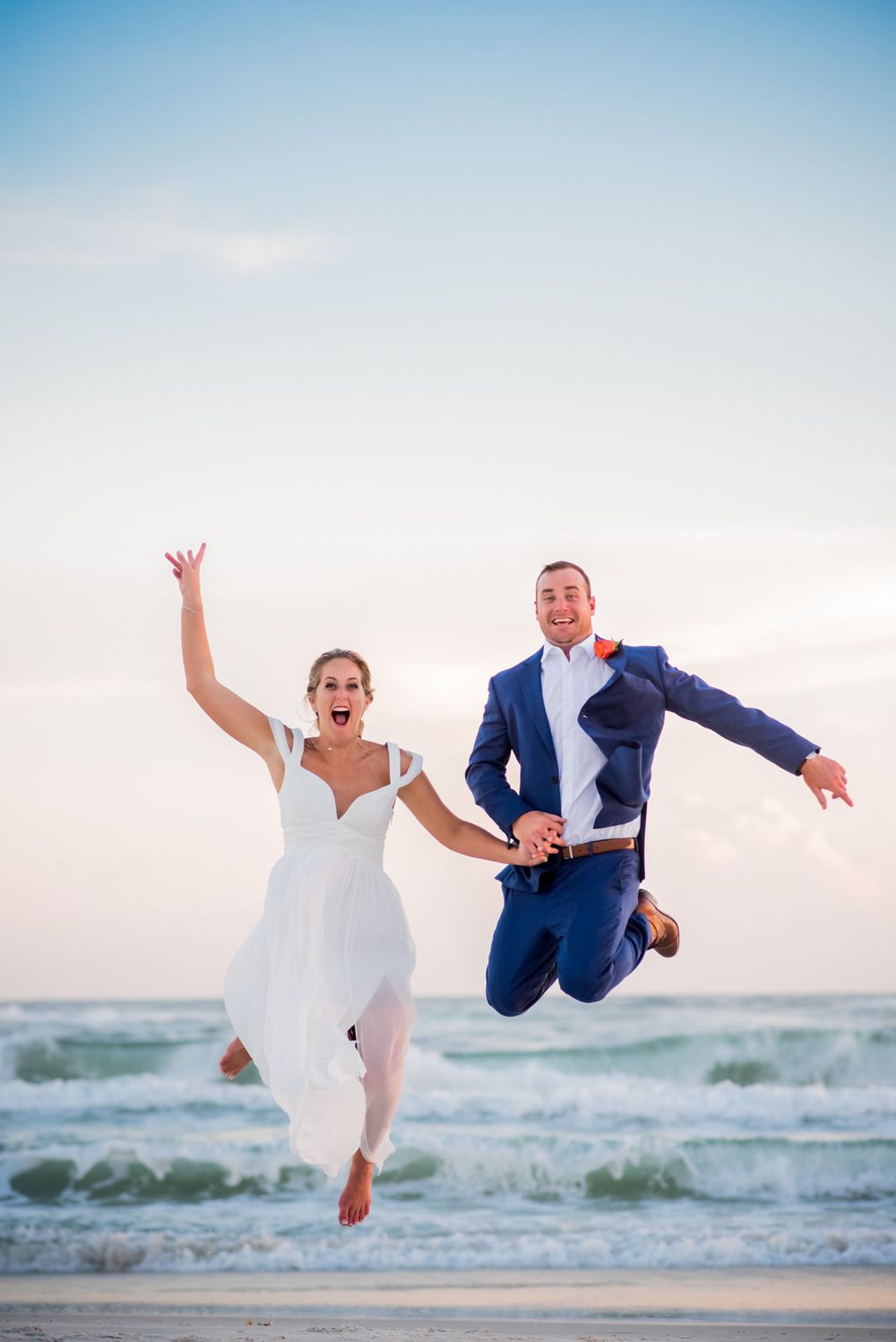 beautifulbride and groom jumping in the air on the beach on their wedding day at sunset on Panama City Beach Florida