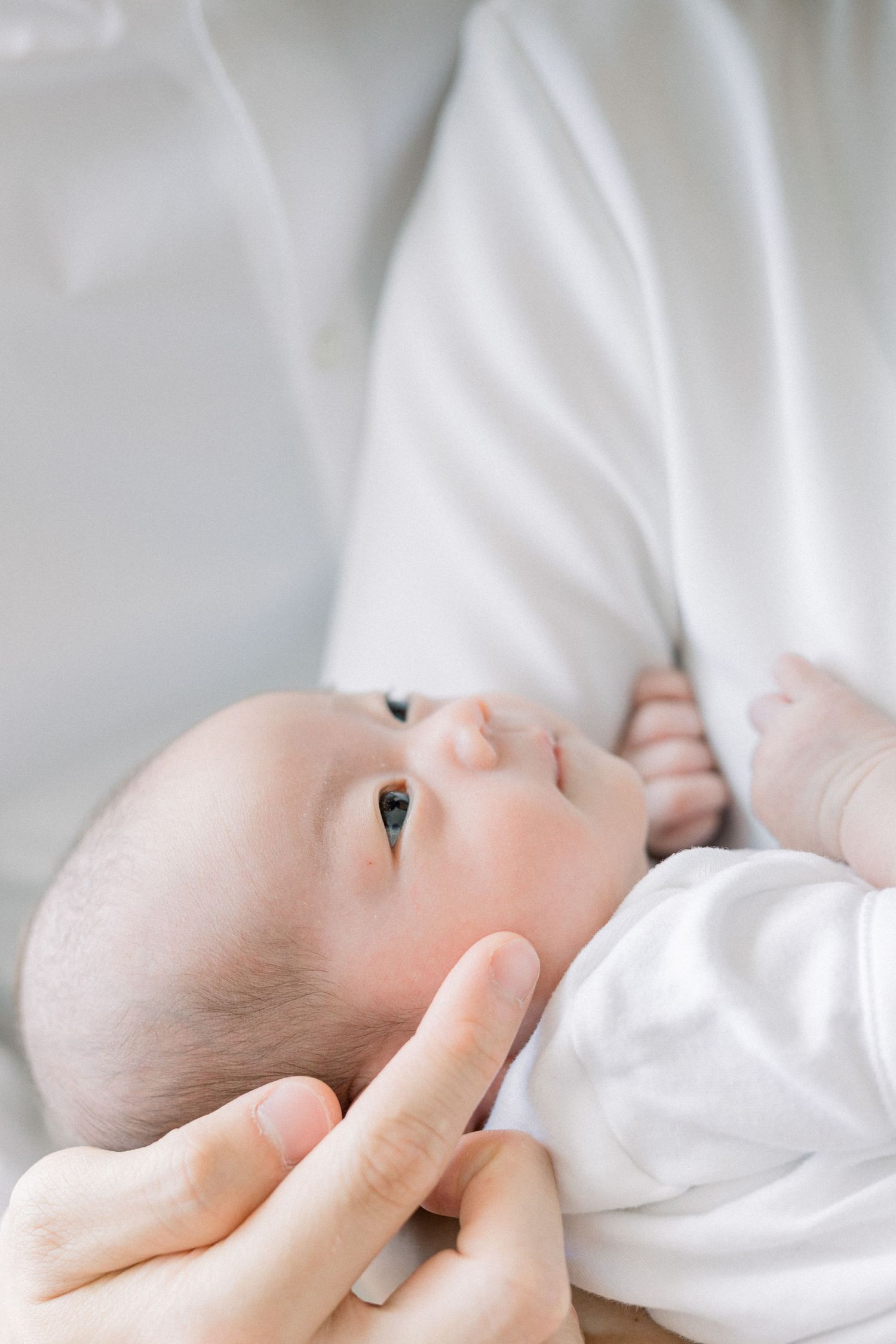 Close-up portrait of a baby in white clothing looking up with gentle expression.