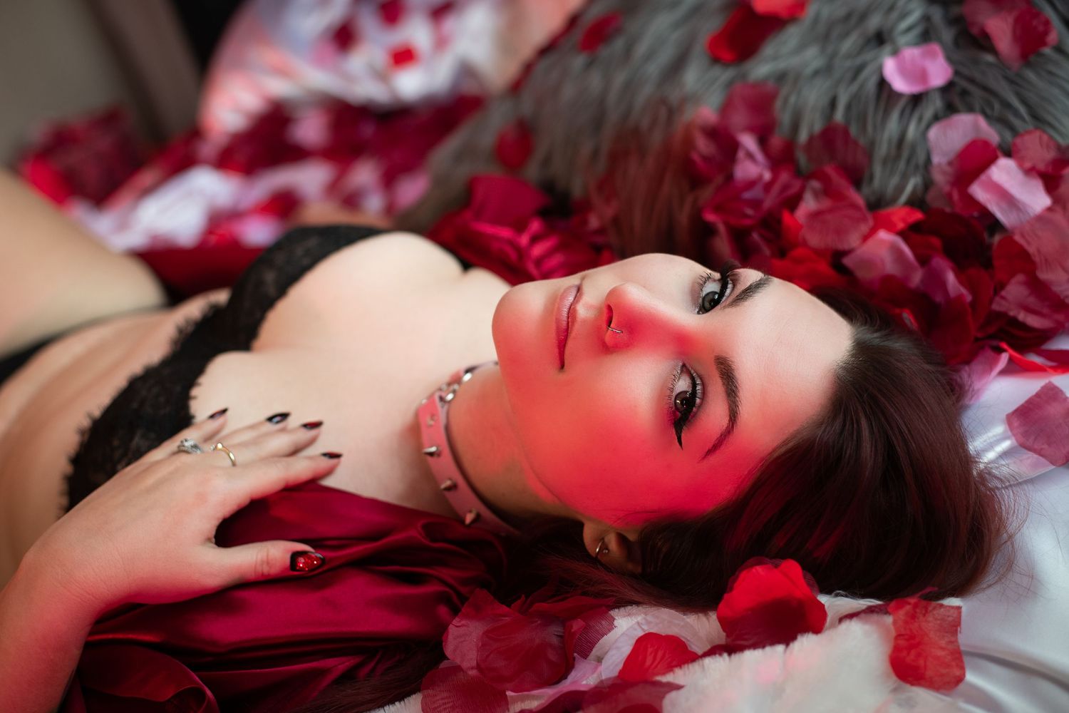 Artistic boudoir photo with red rose petals and dramatic lighting creating a romantic mood.