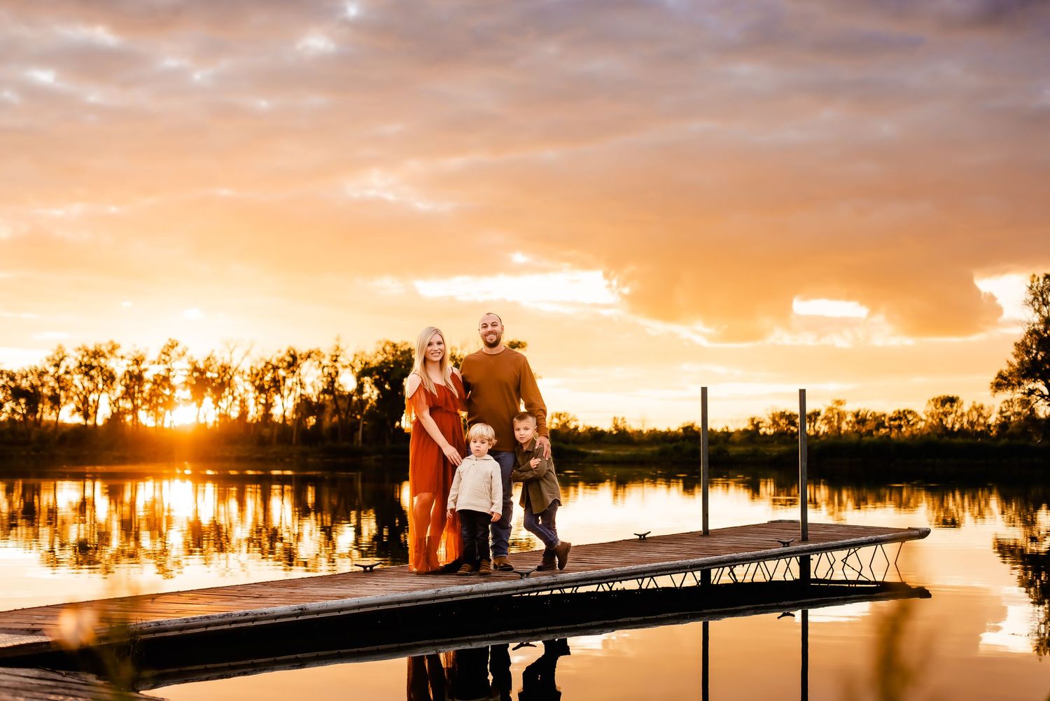 Family silhouettes on a dock during a vibrant orange sunset over a lake.