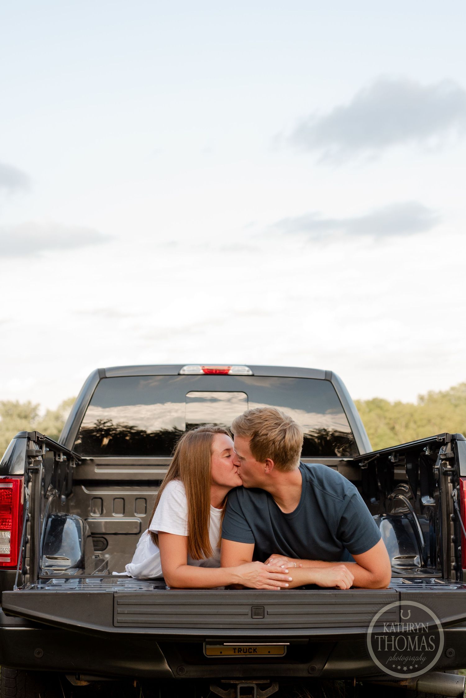 Romantic couple sharing an intimate moment while lying in the bed of a pickup truck at sunset.