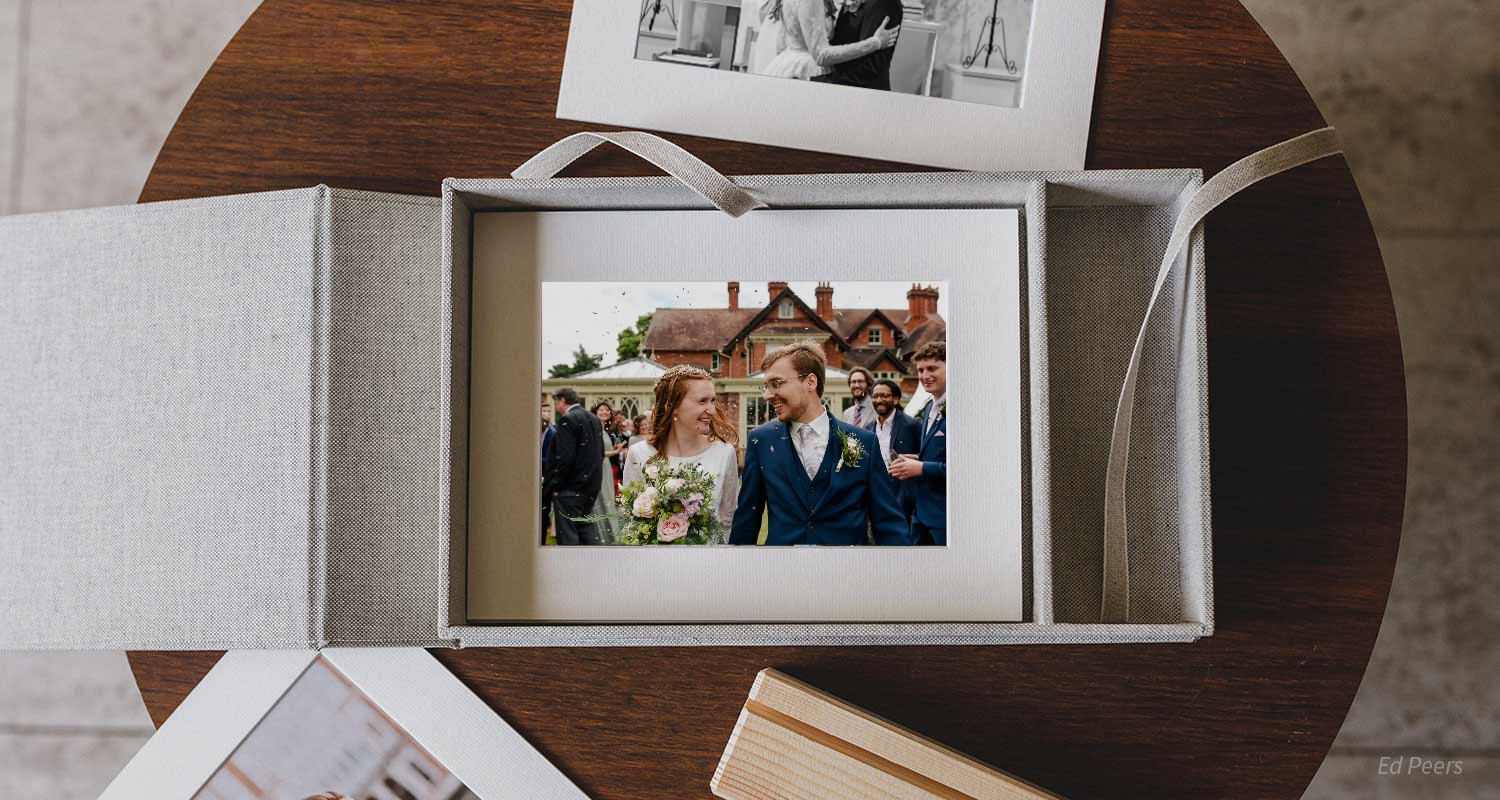 An open wedding album box displaying professional photographs on a wooden table.